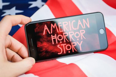 Rusya, St.Petersburg - 11 Nisan 2019: Parmaklar Amerikan bayrağının arka planda Screensaver serisi Amerikan korku hikayesi ile bir akıllı telefon tutun.