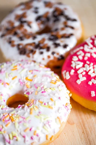 Ahşap arka planda pembe, beyaz ve kahverengi sırlı donutlar. — Stok fotoğraf