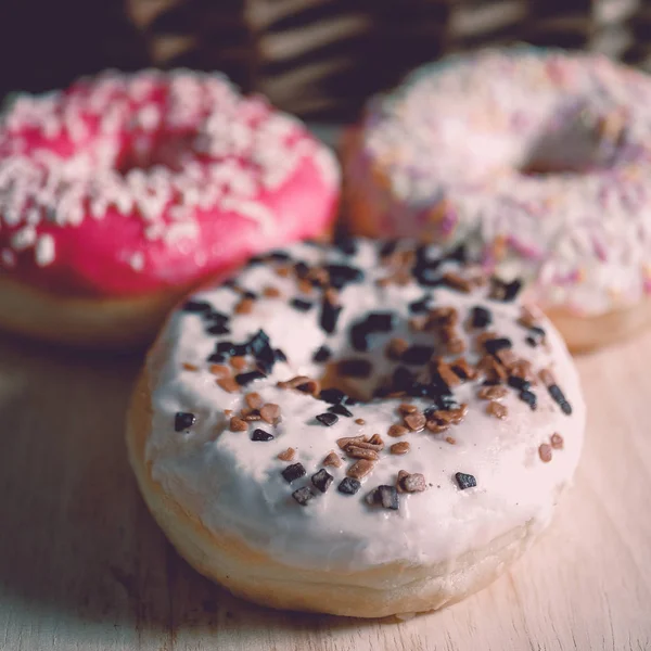 Beyaz, pembe ve kahverengi donutlar ahşap arka planda ve rattan sepetinin yanında. . — Stok fotoğraf