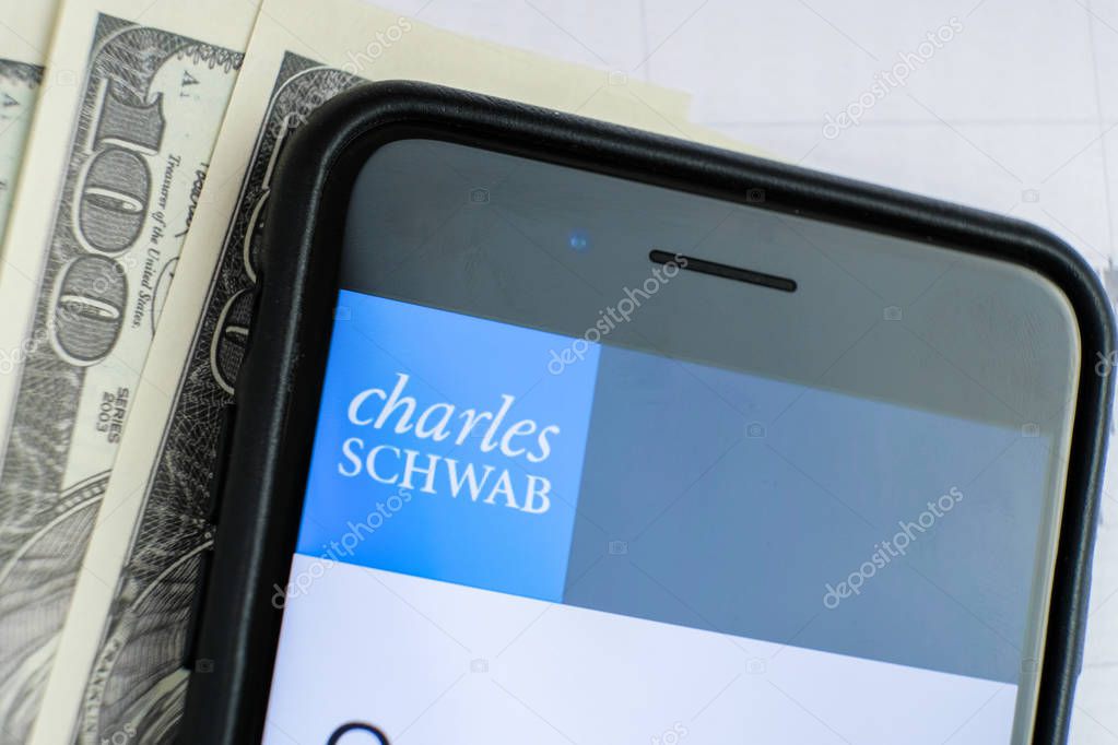 RUSSIA, ST.PETERSBURG, April 4, 2019: site with Logo of the bank Charles Schwab in the smartphone lying on paper with charts and one hundred dollar bills.