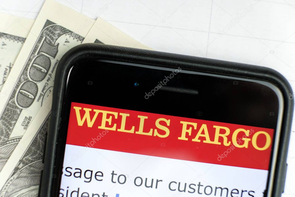 RUSSIA, ST.PETERSBURG, April 4, 2019: site with Logo of the bank Wells Fargo Co in the smartphone lying one hundred dollar bills.