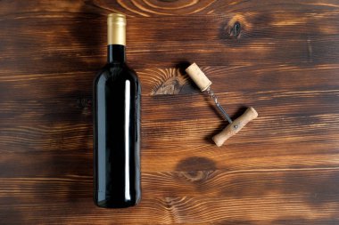 Bir tirbuşon ve ahşap bir arka plan üzerinde merkezinde bükülmüş bir mantar yanında şarap koyu bir şişe.