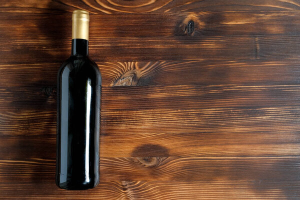 A dark bottle of wine on a wooden background.