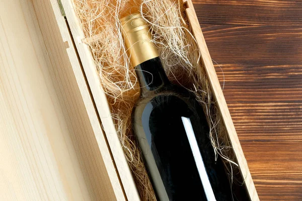 Una botella de vino oscura y cara en una caja de madera sobre un fondo de madera . —  Fotos de Stock