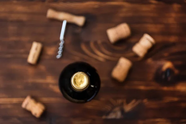 Une bouteille de vin sombre à côté d'un tire-bouchon flou et un bouchon tordu sur un fond en bois . — Photo