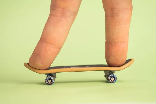 Toets. Man hoplding door twee vingers kleine skateboard op groene achtergrond. — Stockfoto
