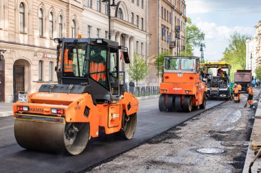 Rusya, St.Petersburg - 12 Mayıs 2019: Yolların onarımı. Turuncu asfalt döşeme, bordo kamyon ve tulum işçileri.