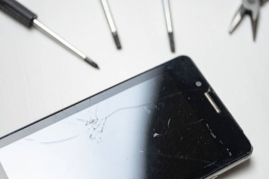 Beyaz arka plan üzerinde tornavida ve çerçeveli kırık ve çatlak ekranlı akıllı telefon.