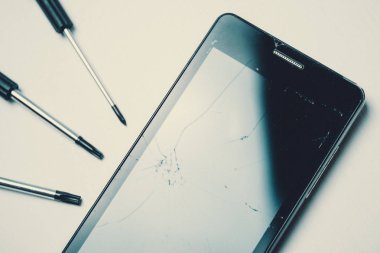 Beyaz arka plan üzerinde tornavida ile kırık ve kırık ekranlı akıllı telefon. Tonda.