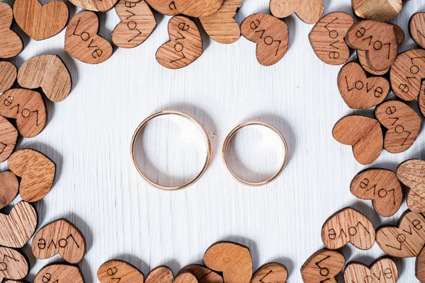 Paar bruiloft gouden ringen omlijst door houten harten op witte achtergrond. Overhead schot. — Stockfoto