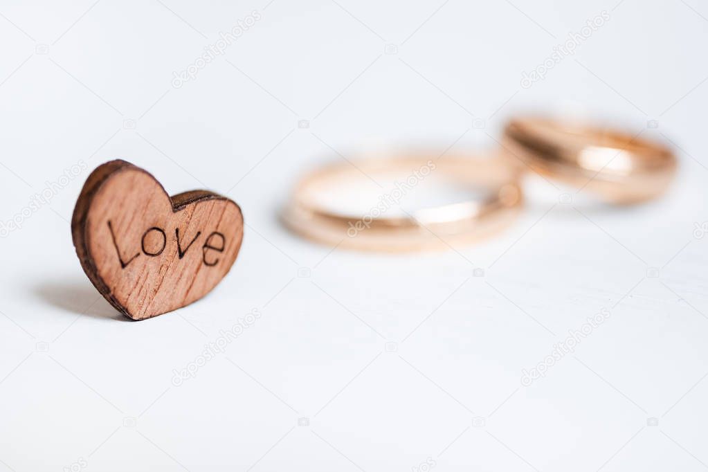 Wooden heart with inscription Love and pair wedding rings on white background. Side view.