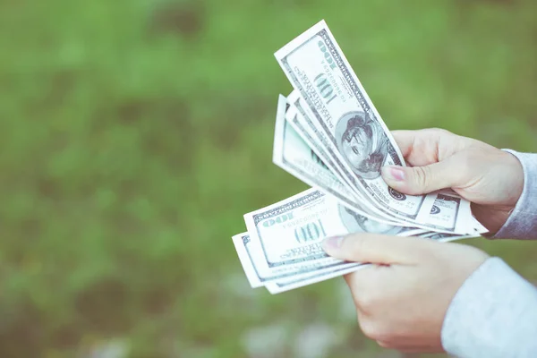 Închide mâinile numărând bancnote de 100 de dolari pe iarba de fundal . — Fotografie, imagine de stoc