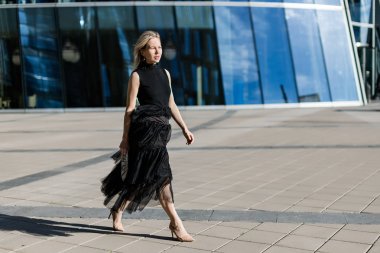Güzel sarışın kız modern bir iş binasının arka planda siyah bir gece elbisesi içinde yürüyor.