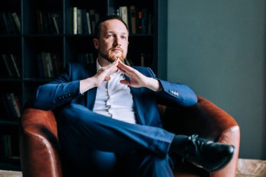 bir takım elbiseli başarılı işadamı katlanmış kollar ile sandalyesinde oturuyor.