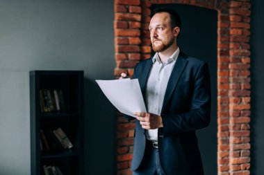 bir takım elbise başarılı işadamı duruyor ve kağıt üzerinde bir mali rapor tutar.