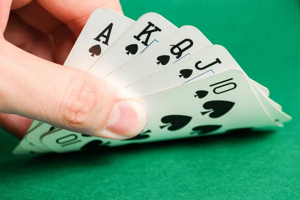Hand holds a combination in poker - royal flush on a green background.