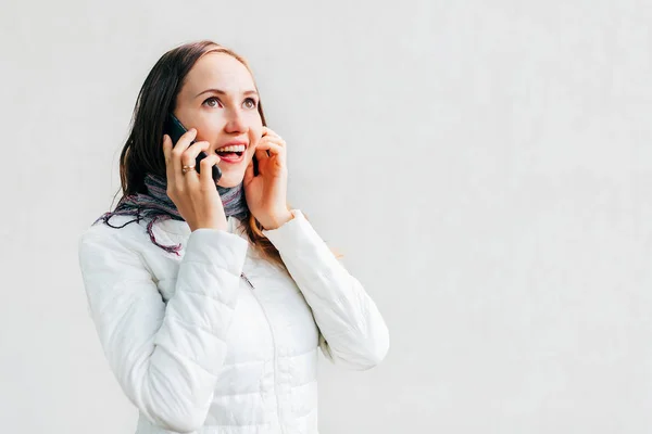 Ενθουσιώδης Καυκάσιος νεαρή γυναίκα με λευκό μπουφάν μιλά από το κινητό τηλέφωνο. Καλά νέα.. — Φωτογραφία Αρχείου