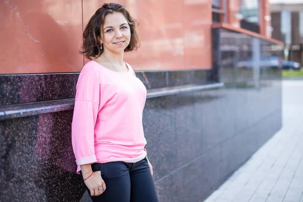 Gülümseyen genç Kafkas kadın arka plan modern bina duvarında objektife bakıyor.