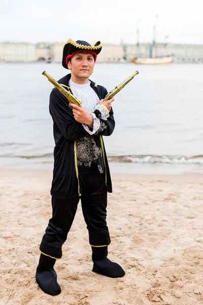 Korsan kostümlü beyaz adam önünde silahla kollarını çapraz.