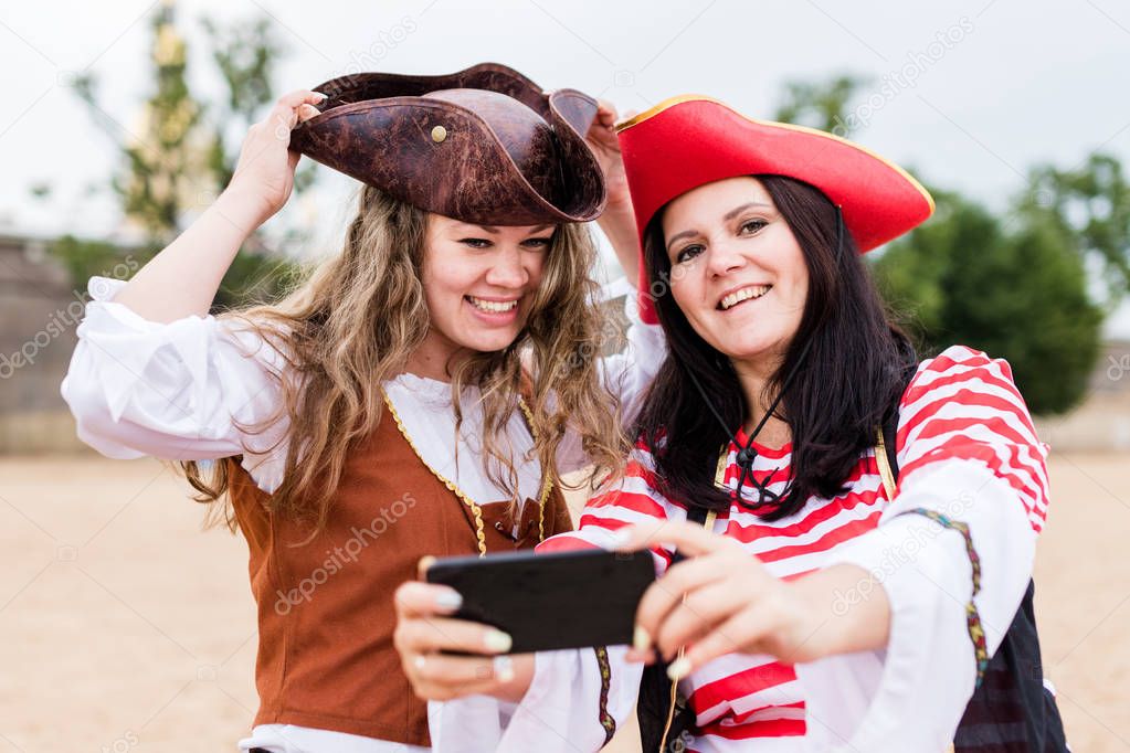 Two young happy smiling Caucasian women in pirate costumes taking selfie on smartphone.
