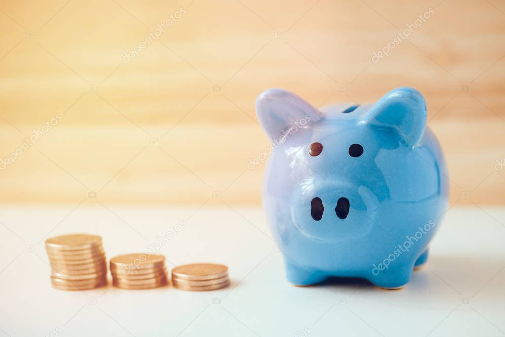 Piggy bank with piles of coins on a white and wooden background.