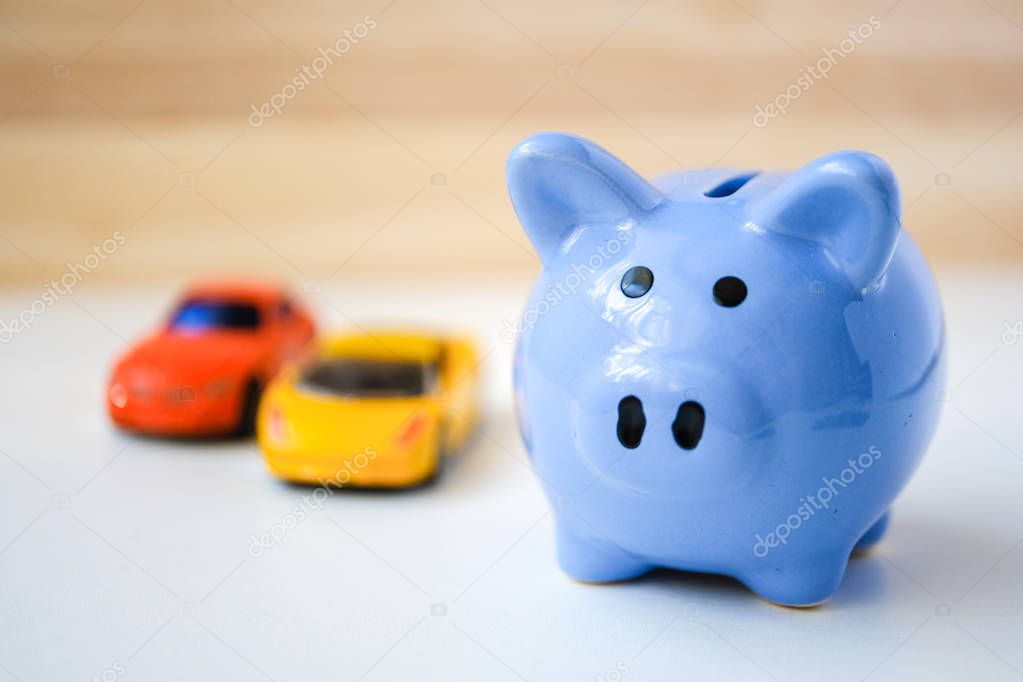 Piggy bank and two toy cars on white and wooden background.