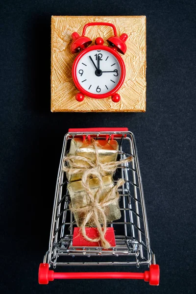 검은 종이 배경에 빨간 시계가있는 선물이있는 트롤리. 크리스마스 쇼핑 컨셉. — 스톡 사진