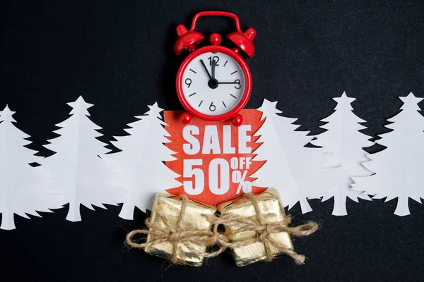 Relógio vintage com caixas de presente em uma placa de desconto vermelho com um envelope de artesanato e papel árvores de Natal em um papel whatman preto. Conceito de venda de Natal . — Fotografia de Stock