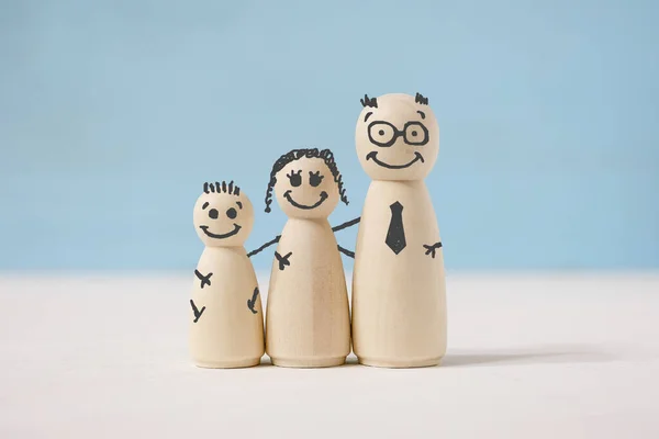 Houten figuren familie met geschilderde gezichten, handen op blauwe achtergrond. — Stockfoto