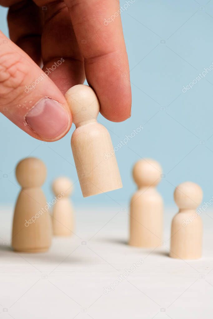 A hand holds a wooden figurine on a blue background. Team building concept. Close up.