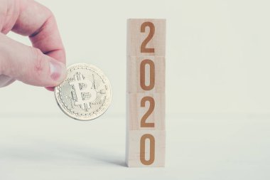Bitcoin, beyaz arka planlı tahta küplerde 2020 numarayla el ele tutuşuyor. Değişikliklerin başarısı yeni yılda kripto para birimi.