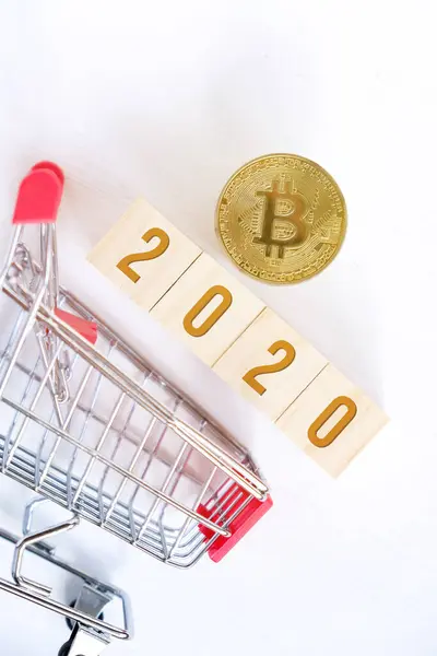 Bitcoin mit Zahlen 2020 auf Holzwürfeln auf weißem Holzgrund mit einem Trolley. Erfolg beim Kauf von Kryptowährungen im neuen Jahr. Vertikal. flache Lage. — Stockfoto