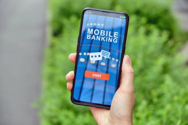 Mobil bankacılık arayüzü ve simgelerle iletişim kurmak için bir sohbet düğmesi olan akıllı telefonu elinde tut.