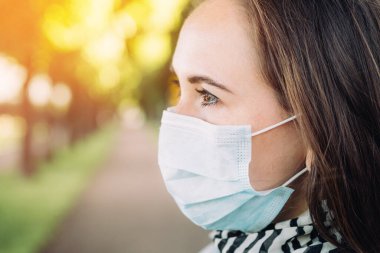 Parkta yüzünde tıbbi maske olan güzel beyaz bir kızın portresi. Bir salgın sırasında yeni normallik ve yaşam