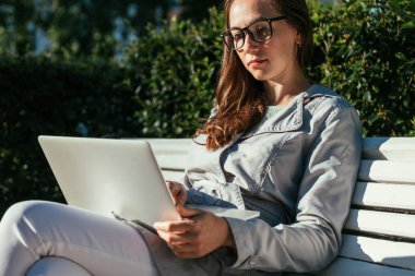 Kafkas öğrenci kız elinde dizüstü bilgisayarla parkta oturuyor ve uzaktan çalışıyor.