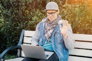 Beyaz bir adam parkta bir bankta oturur ve bilgisayardaki görüntülü sohbet yoluyla iletişim kurar..