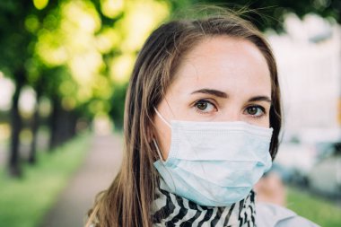 Park arka planında tıbbi maske takmış 30 yaşında beyaz bir kızın portresi..