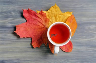 Sonbahar kurutulmuş yapraklar ve ahşap arka planda bir kupa çay..