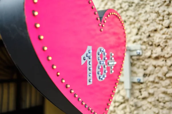 Advertising sign of a shop on the street in the shape of a heart with the designation of age 18