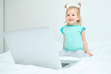 Şanslı çocuk laptopun yanındaki yatakta çömeliyor.