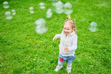 Mutlu çocuk bir yaz parkında sabun köpüğü kovalıyor.