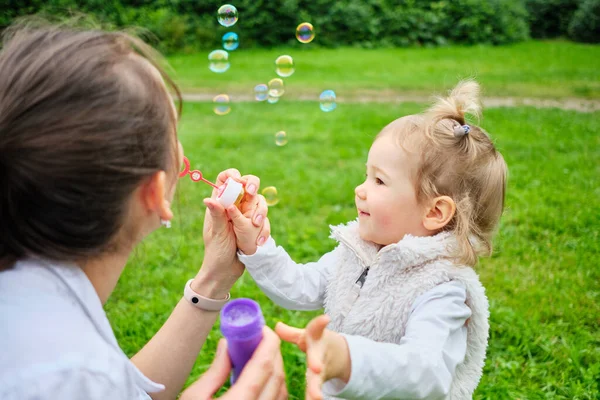 Happy toddler and mom make soap bubbles in a summer park