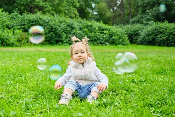 Uma Criança Sorrindo Senta Grama Parque Verão Olha Para Bolhas — Fotografia de Stock