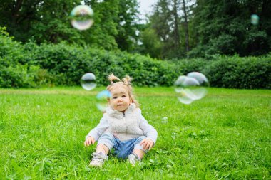 Kafkasyalı bir çocuk çimenlerde oturur ve sabun köpüklerine bakar..