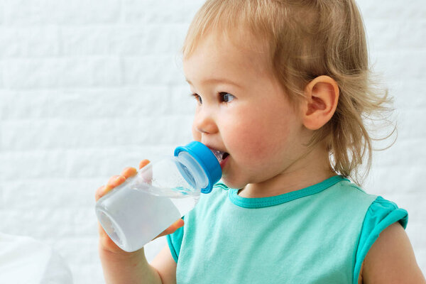 Child holds a plastic water bottle and drinks.