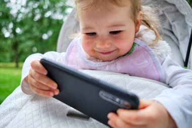Beyaz çocuk bebek arabasında oturuyor ve akıllı bir telefonla oynuyor..