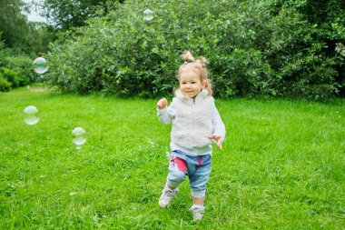 Beyaz çocuk parkta sabun köpüğü üflüyor..