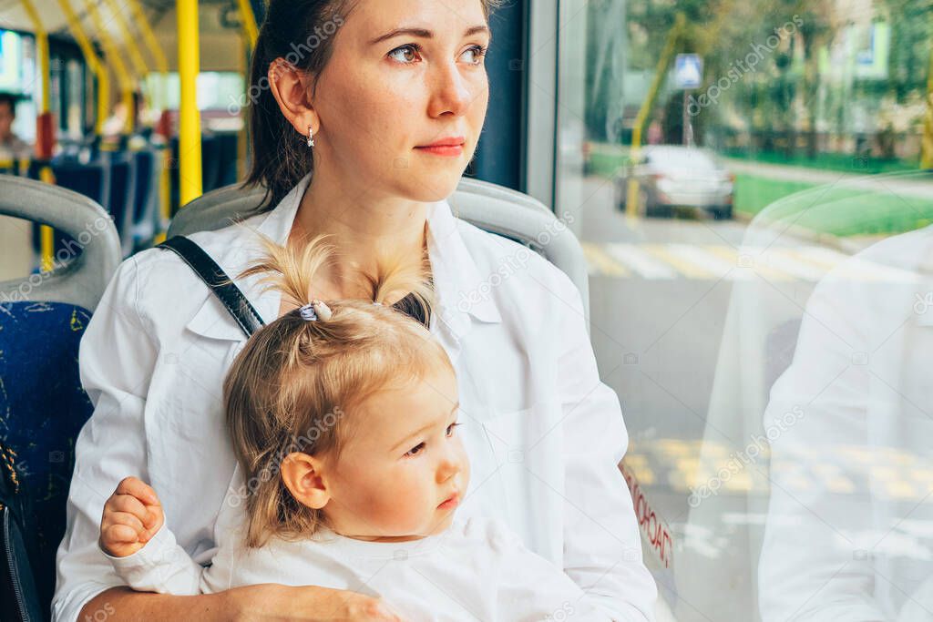 Caucasian toddler looking out the window of public bus with mom.
