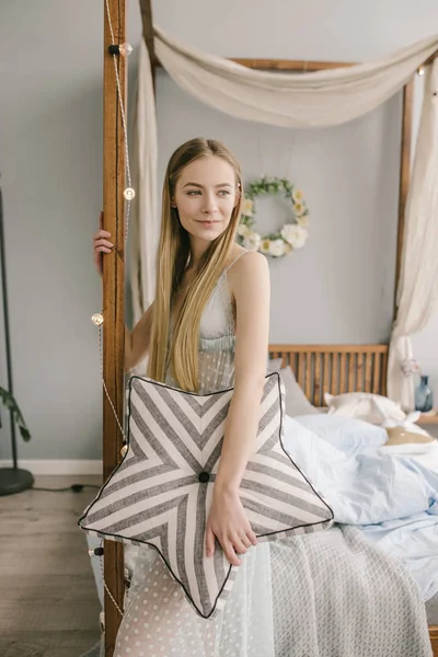 Beautiful young woman wearing pajamas in bed at home is holding a pillow — Stock Photo, Image