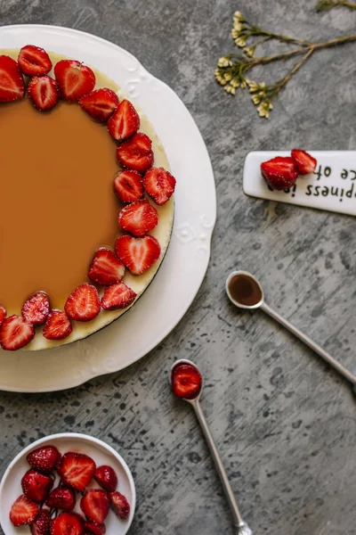 Çilek ve vanilya krem peynir pasta. Karamel ve berry ve çilek ile küçük tabak kaşık gri arka plan üzerinde olduğunu. Yukarıdaki fotoğraf